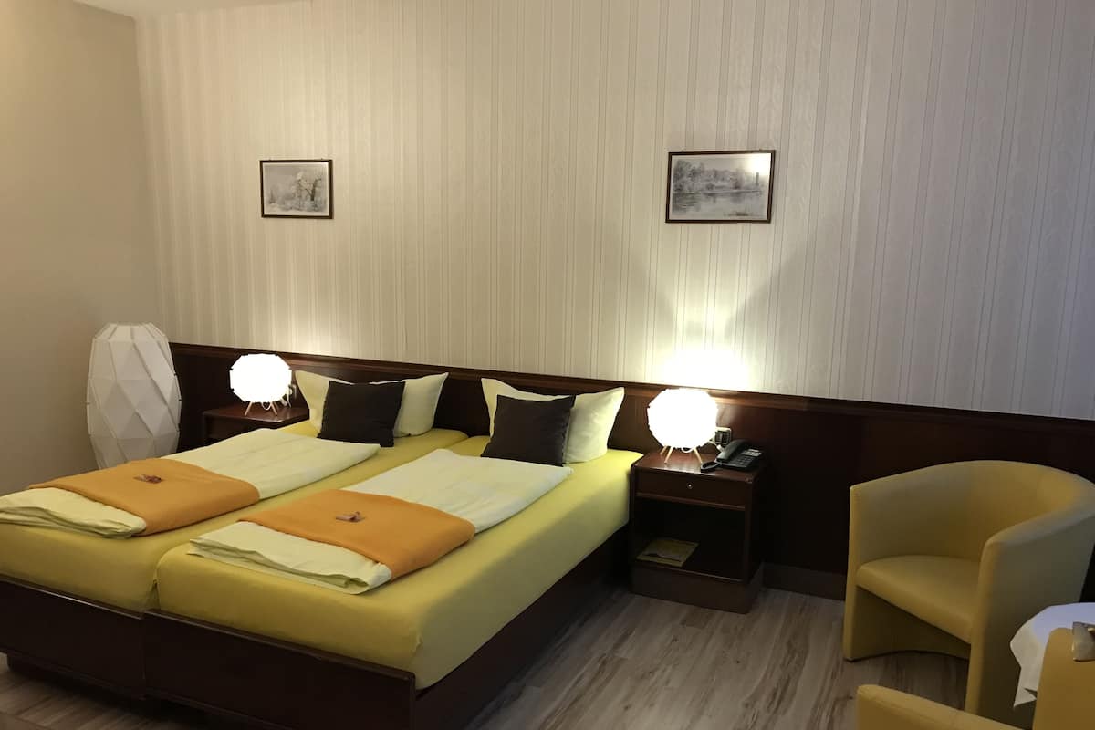Une chambre d’hôtel avec un lit double, deux tables de chevet avec des lampes, une chaise et deux tableaux encadrés au mur.
