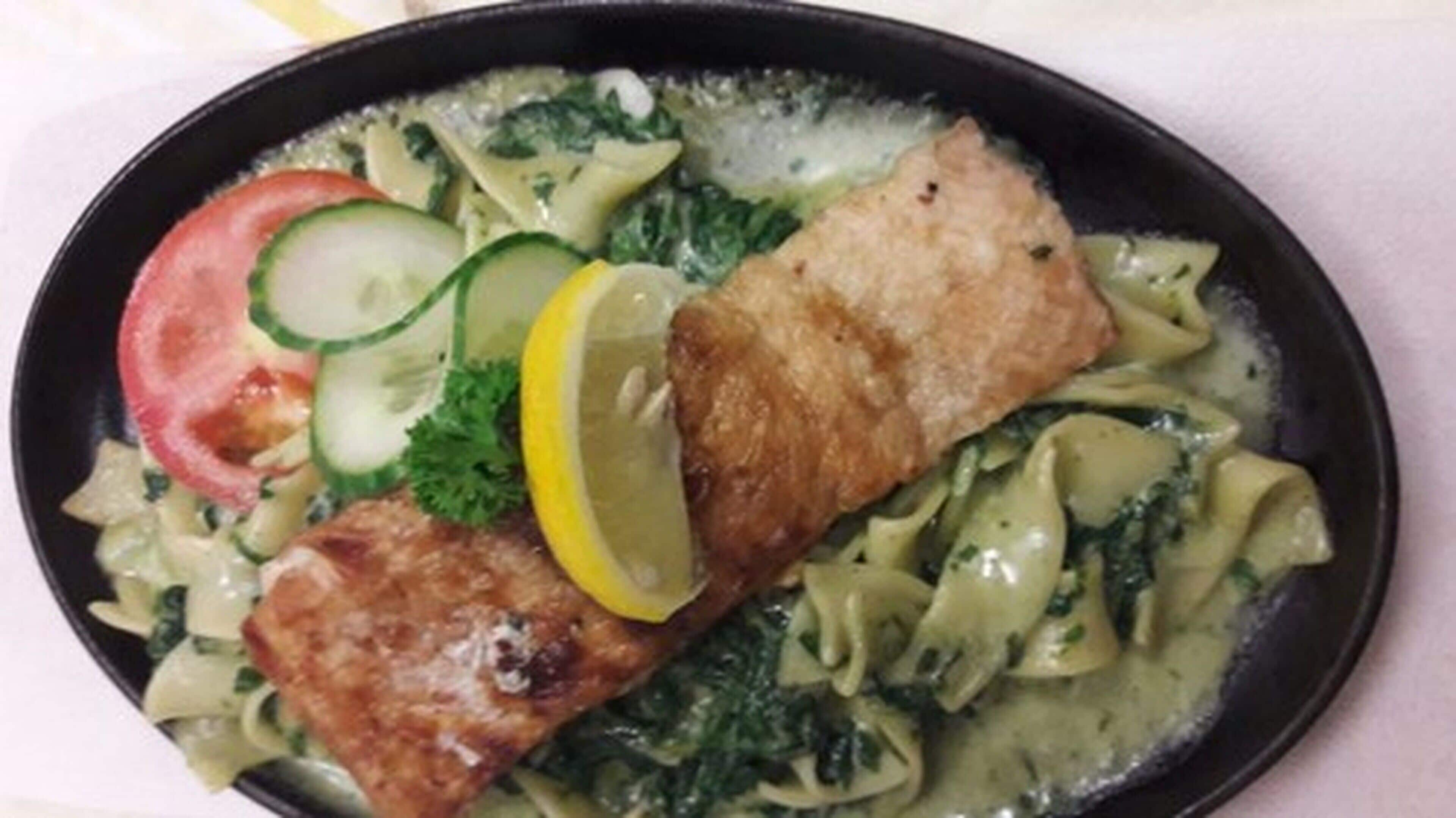 Une assiette contenant un morceau de poisson, des pâtes, une tranche de tomate et quelques légumes verts.