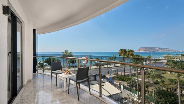 A balcony with a table and chairs, offering a view of the sea and a distant island. - Grand Uysal Beach&Spa Hotel - All inclusive (Alanya)