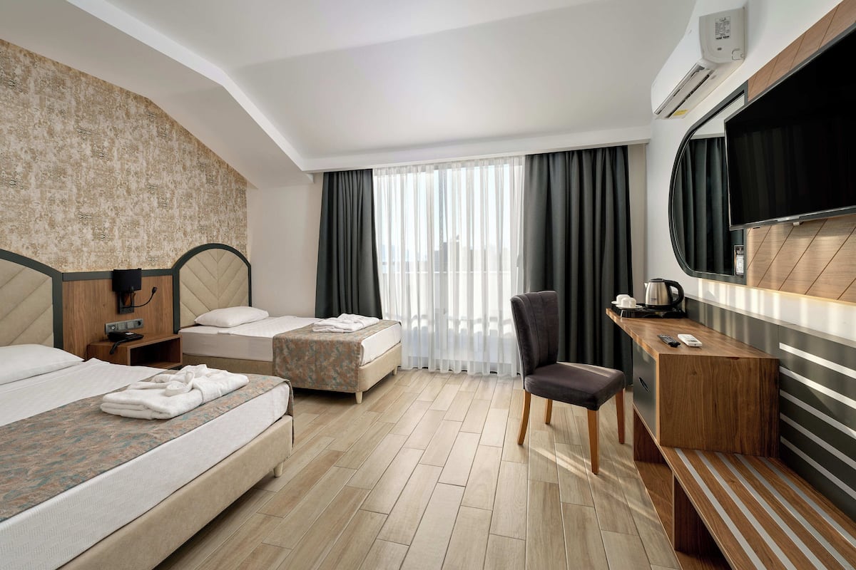 A hotel room with two beds, a desk, a chair, a TV, and a window with curtains.