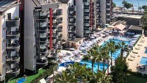 A high-rise hotel with multiple balconies, a swimming pool, and a view of the ocean. - Grand Uysal Beach&Spa Hotel - All inclusive (Alanya)