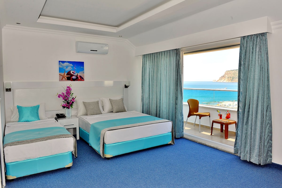 A hotel room with two beds, a small table with drinks, a chair, and a view of the sea.