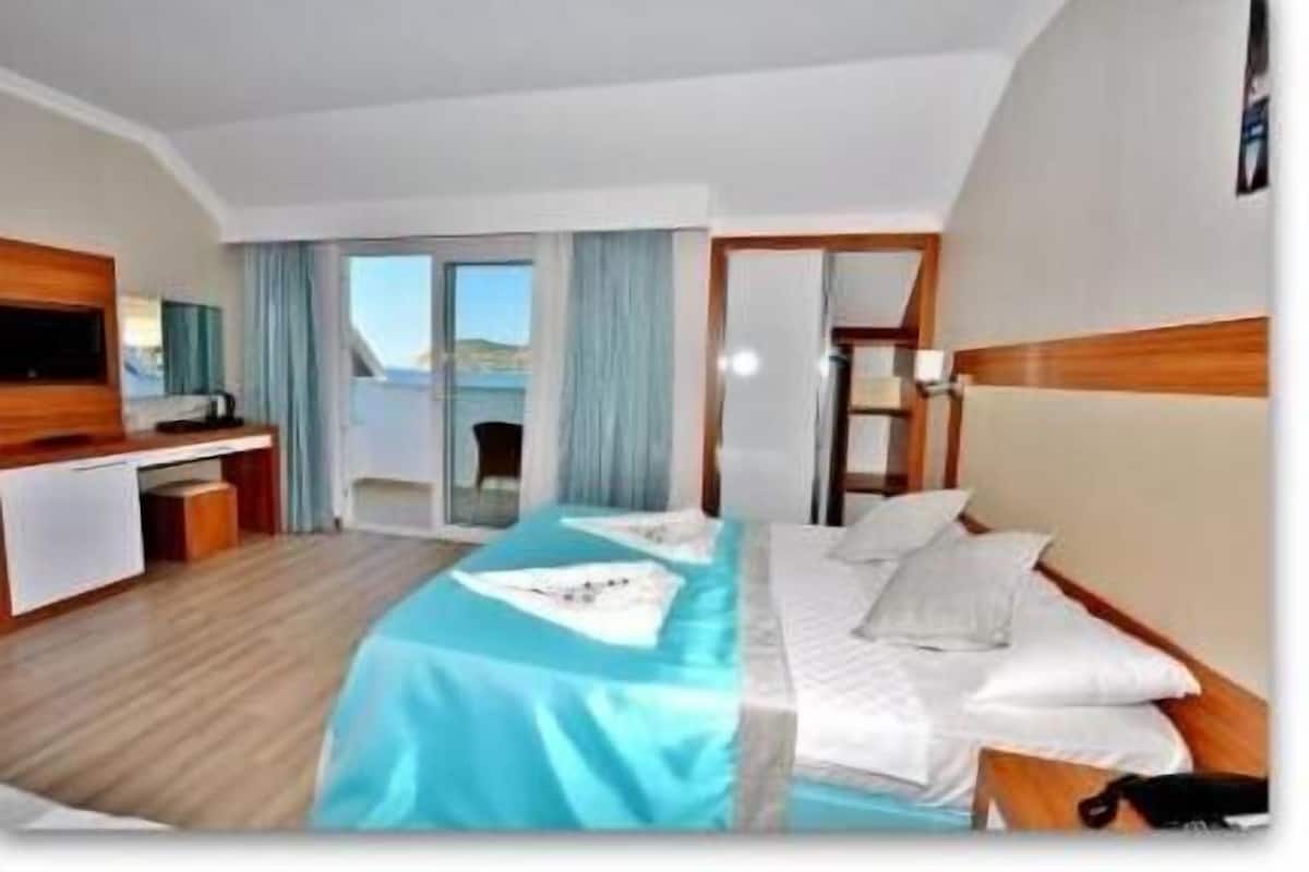A hotel room with a bed, a desk, a chair, and a view of the sea.