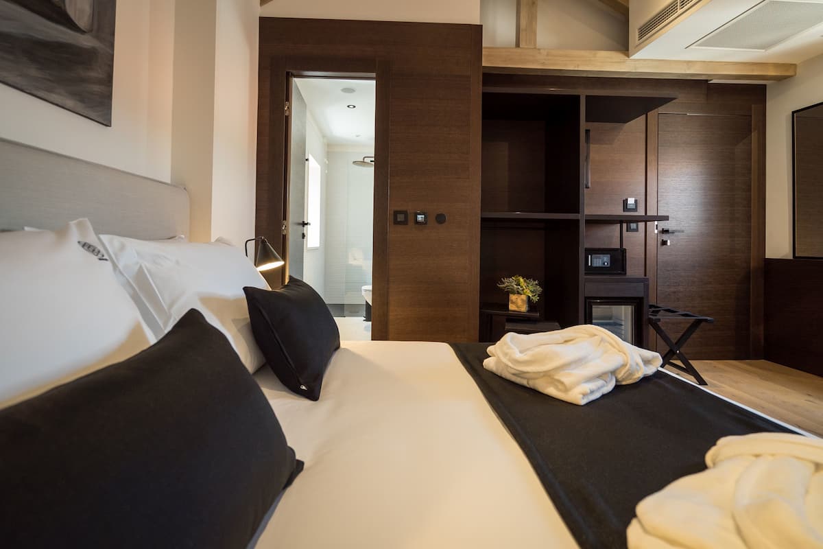 A modern hotel room with a large bed, a bedside table with a lamp, a small plant, and a built-in safe.