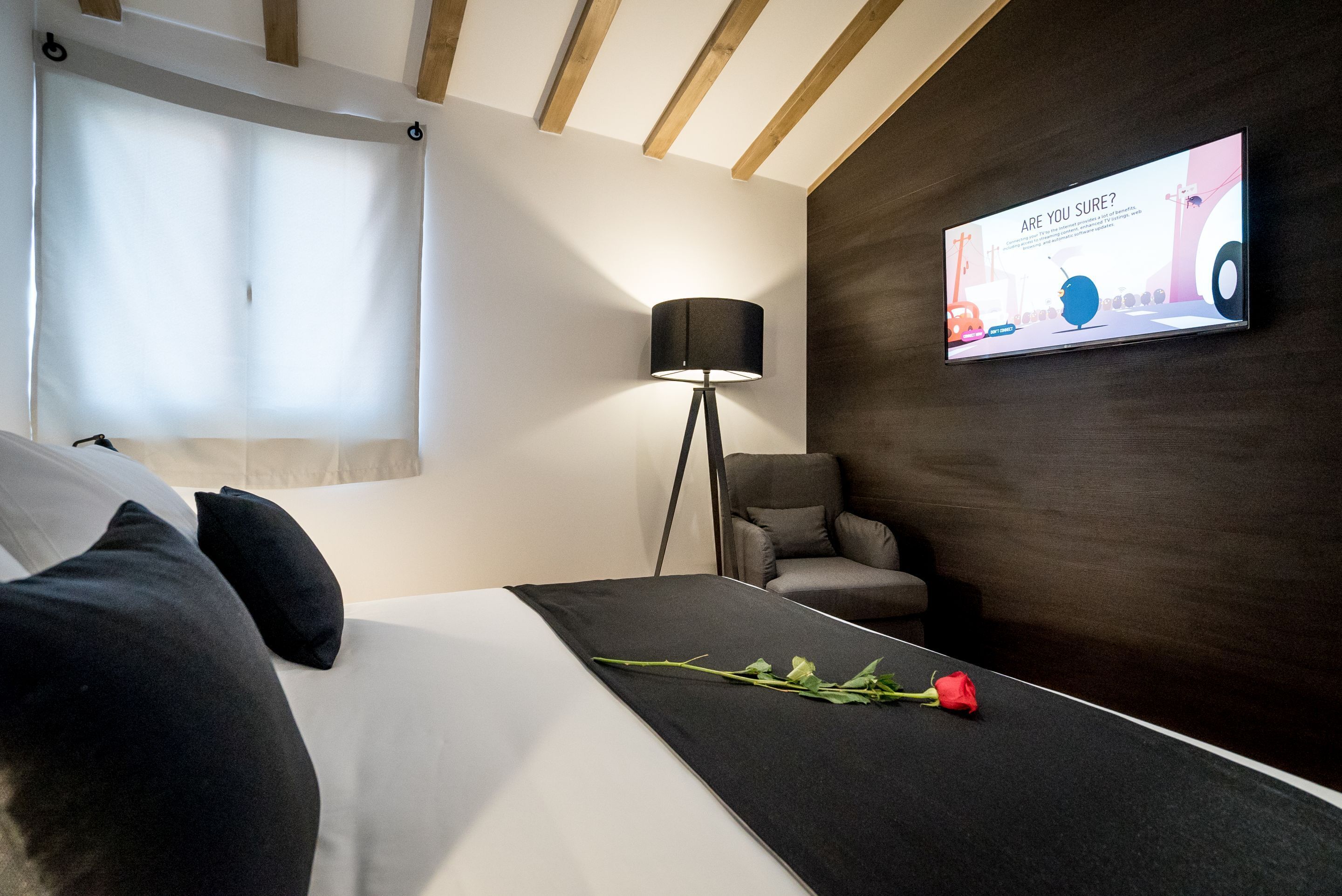 A modern hotel room with a bed, a desk, a lamp, a chair, and a TV displaying a message.