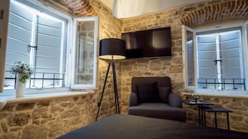 Un dormitorio con paredes de piedra, una cama, un televisor montado en la pared y un ventanal con vistas.