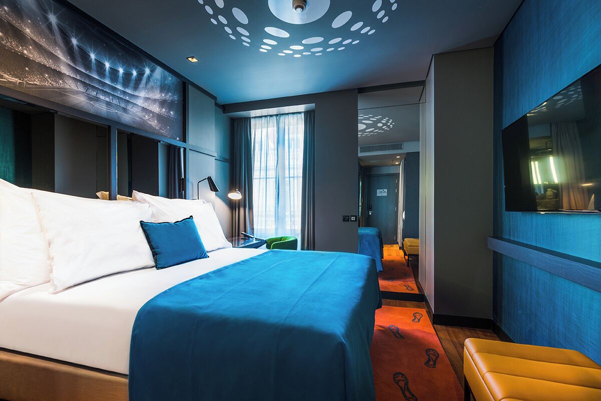 A hotel room with a large bed, a seating area, and a view of the hallway.