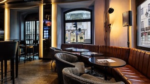 Un espacio acogedor de bar con asientos de cuero, sillas de mimbre y pequeñas mesas redondas.