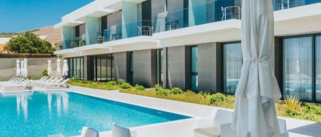 A modern hotel with a pool, white outdoor furniture, and a covered seating area.