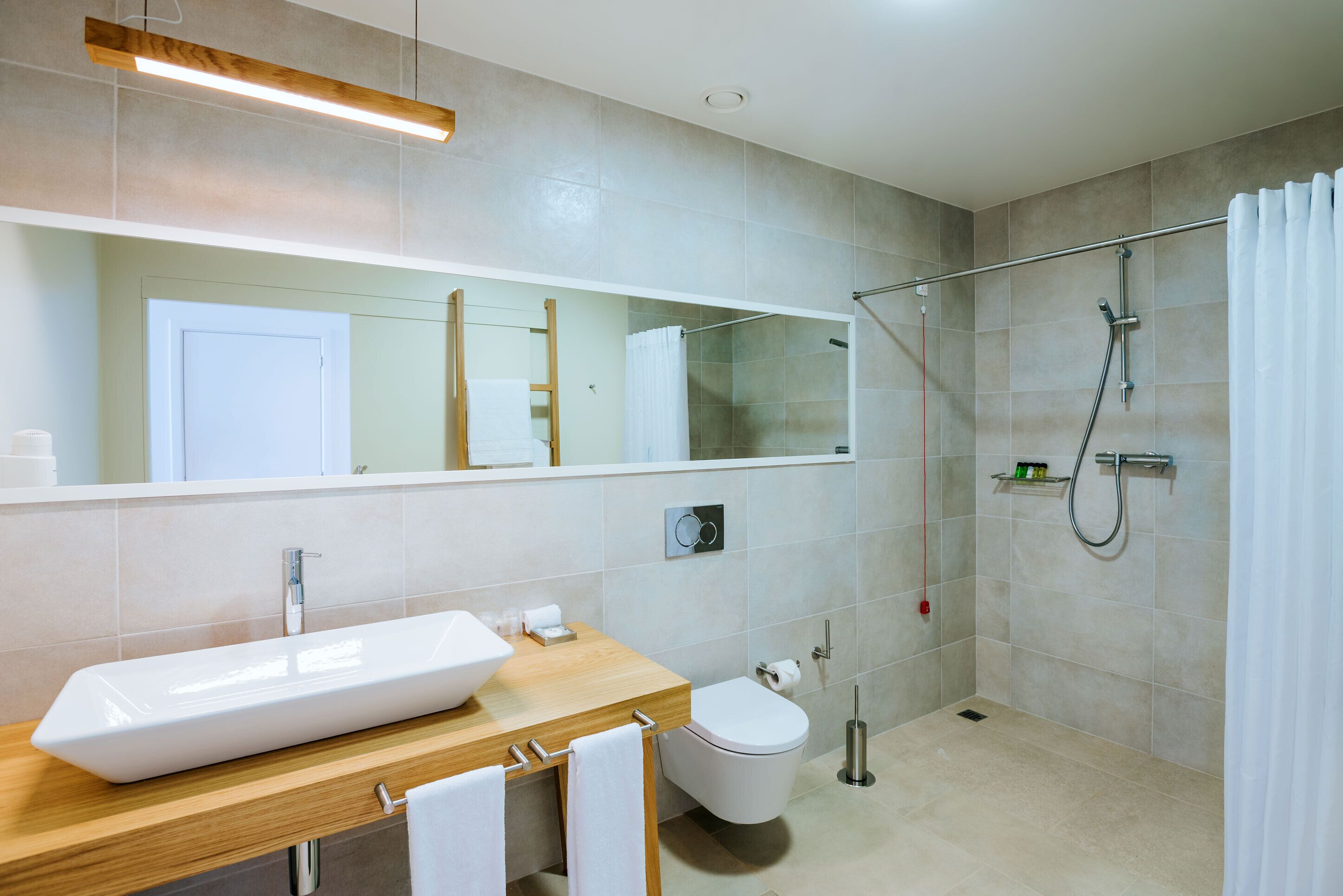 A modern bathroom with a wooden vanity, a large mirror, a white sink, a toilet, and a glass-enclosed shower area.