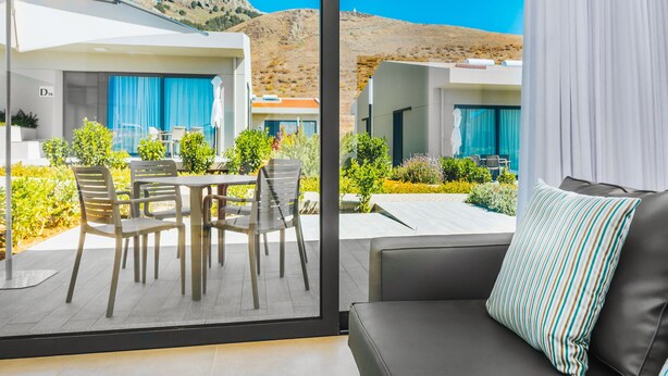 Una habitación de hotel moderna con balcón, amoblada con un sofá y sillones, y vista a un paisaje montañoso.