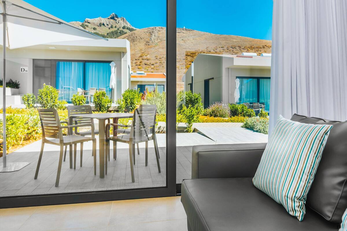 Une chambre d’hôtel moderne avec balcon, comprenant un canapé et des fauteuils, et offrant une vue sur un paysage montagneux.