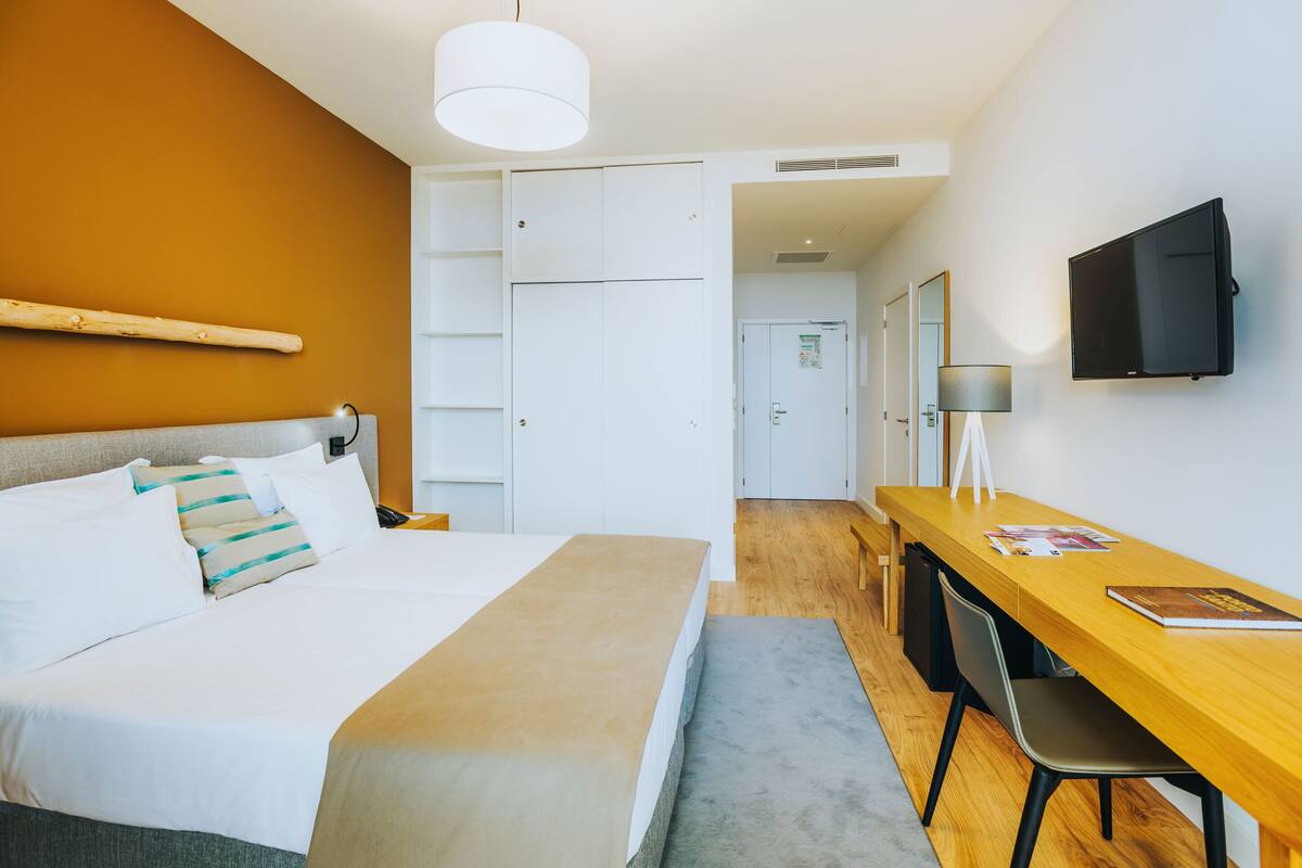 Une chambre d’hôtel comprenant un lit, un bureau, une chaise, une télévision et une armoire.