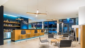 Zona de bar moderna con una barra de madera, taburetes y una variedad de botellas de licor.