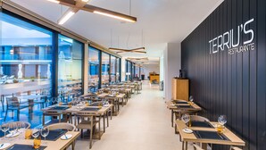 Interior moderno de restaurante con mesas largas, sillas y un amplio ventanal que ofrece vistas al área exterior.