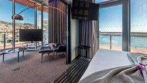 A modern hotel room with a large bed, a TV, a desk, and a chair. It has a view of a bridge and water. - Pestana CR7 Funchal (Funchal)