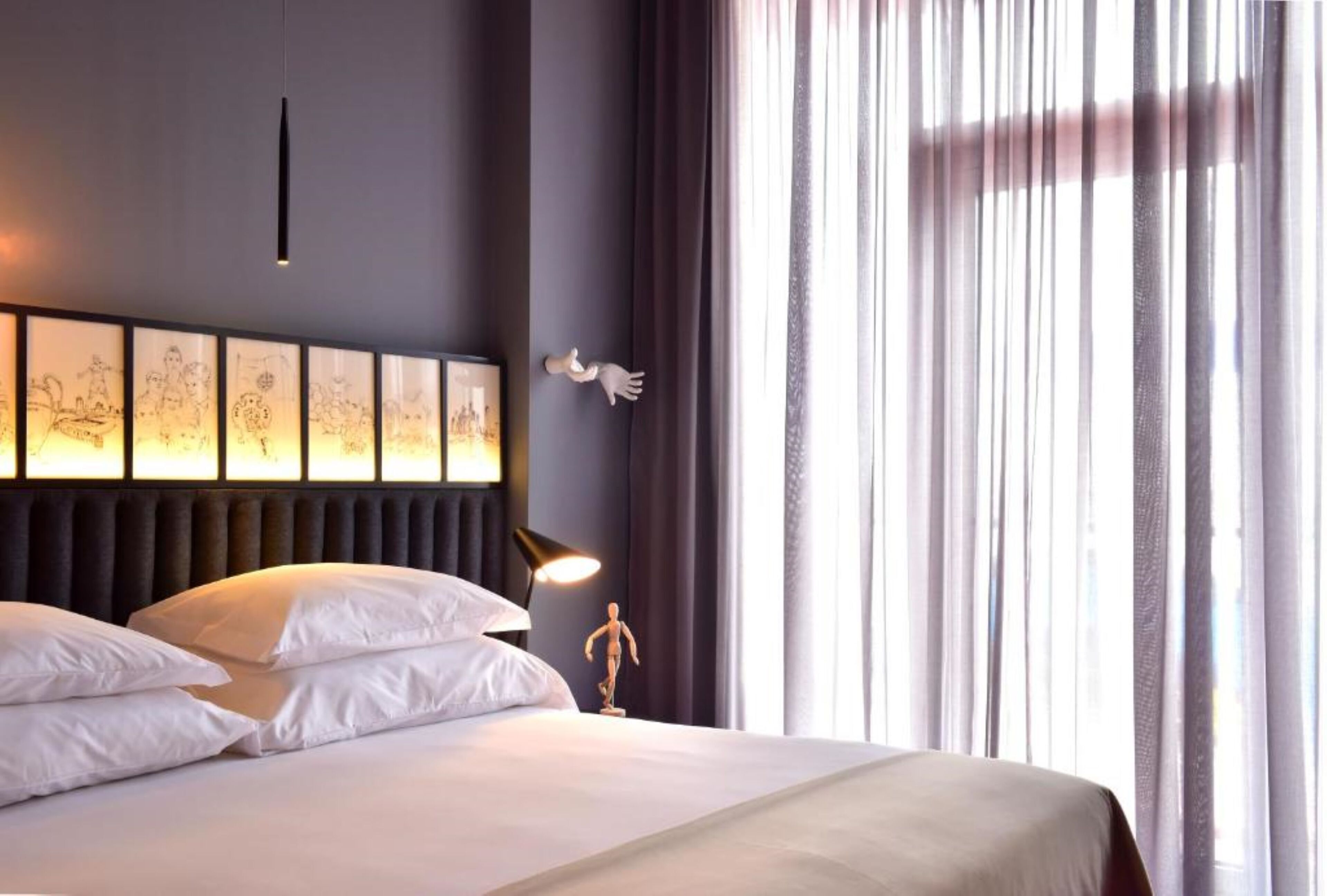 Una camera d'albergo con un letto grande, un comodino con una lampada e una parete decorata con quadri.