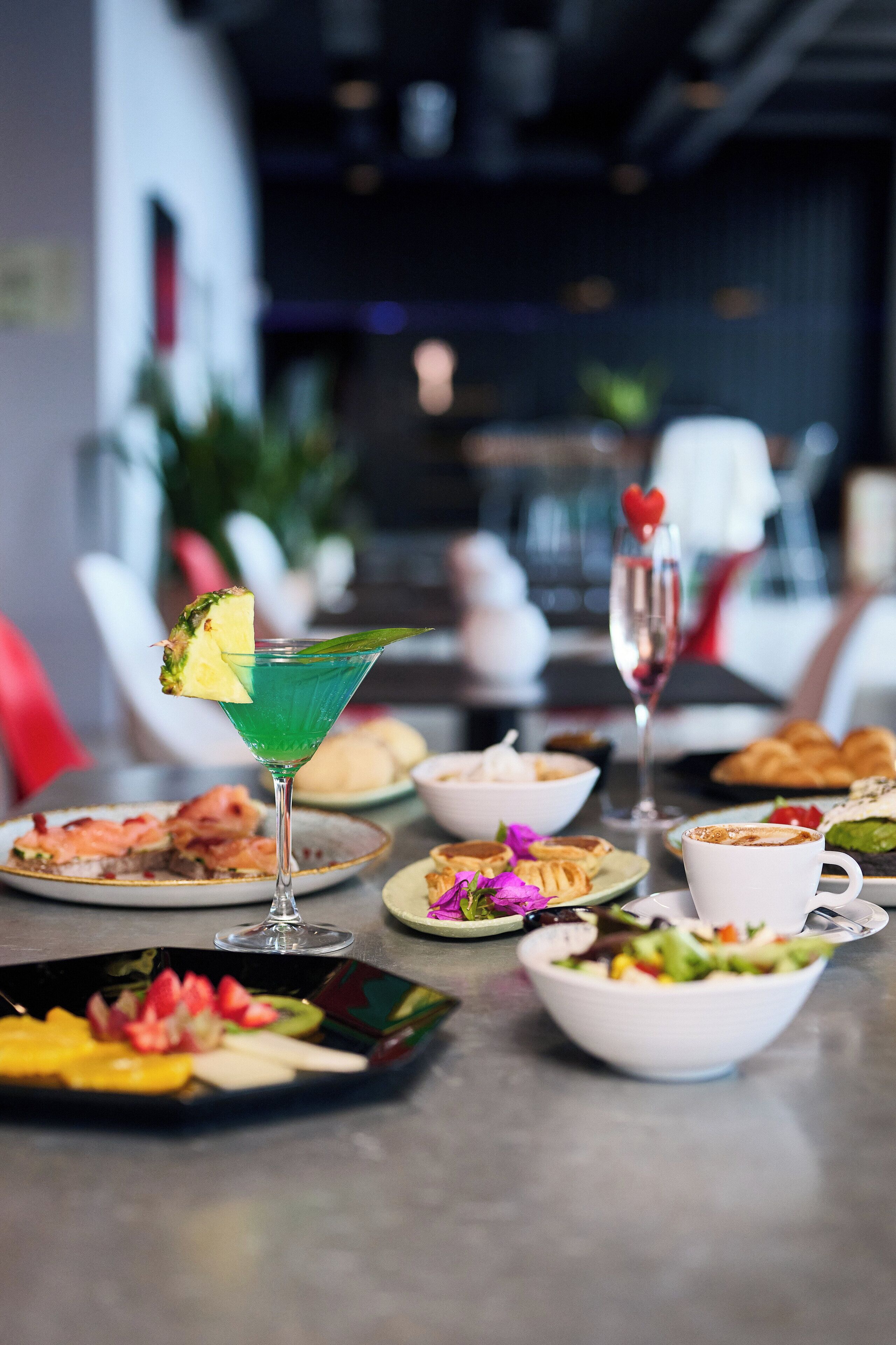 Een eettafel met diverse gerechten, waaronder een groene cocktail, een glas champagne en borden met eten.
