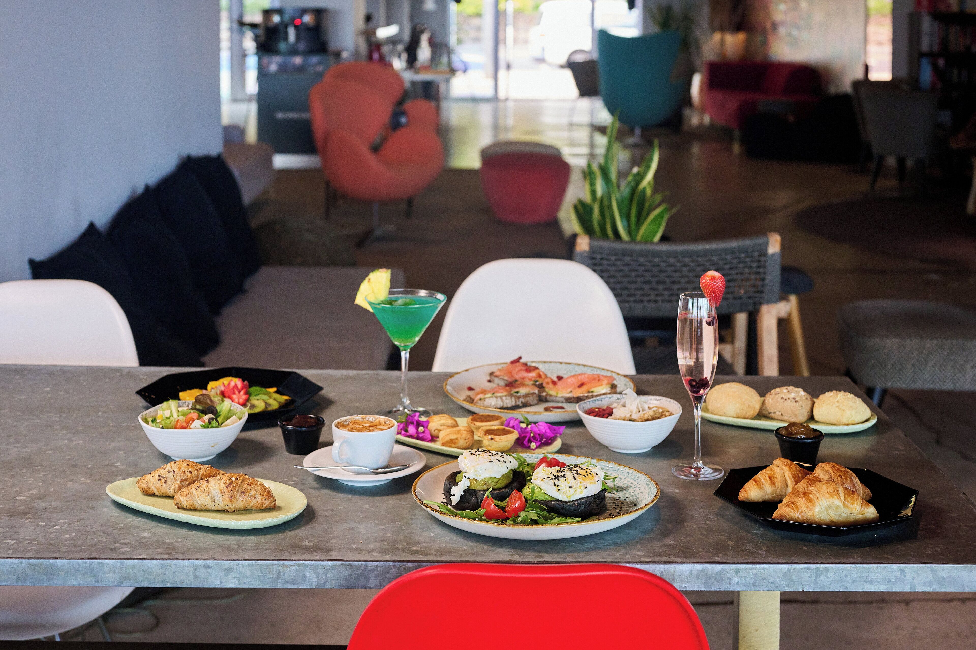 Een eettafel met diverse gerechten, waaronder croissants, een salade en een martini.