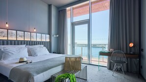 A hotel room with a large bed, a desk with a chair, a view of the water, and artwork on the wall. - Pestana CR7 Funchal (Funchal)