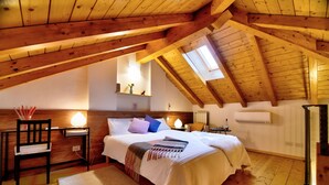 A bedroom with a sloped ceiling, wooden beams, a bed with white bedding, a bedside table with a lamp, and a small shelf with decorative items. - Bed & Breakfast Le Due G (Varese)