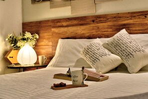 A neatly made bed with a wooden headboard, white pillows with handwritten notes, a bedside table with a lamp, a mug, and a tray with chocolates. - Bed & Breakfast Le Due G (Varese)