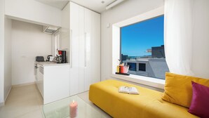 En moderne lejlighed med en gul sofa, et glasbord, et pink lys og udsigt over byen gennem et stort vindue.