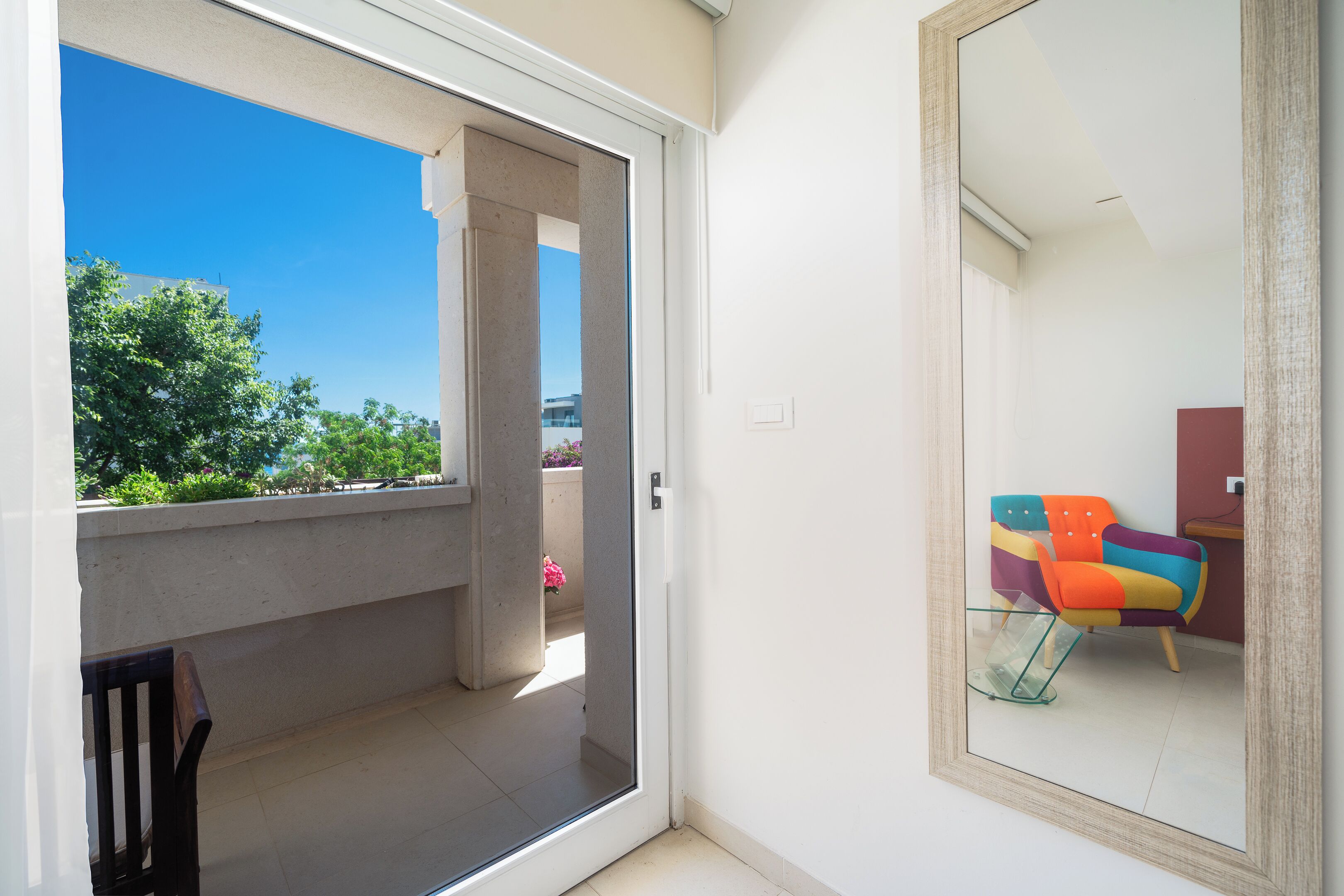 A room with a sliding glass door leading to a balcony, a colorful chair, and a small table.