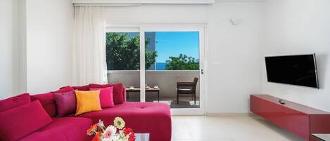 A modern living room with a red sofa, a glass coffee table with flowers, a flat-screen TV, and a sliding glass door leading to an outdoor balcony.