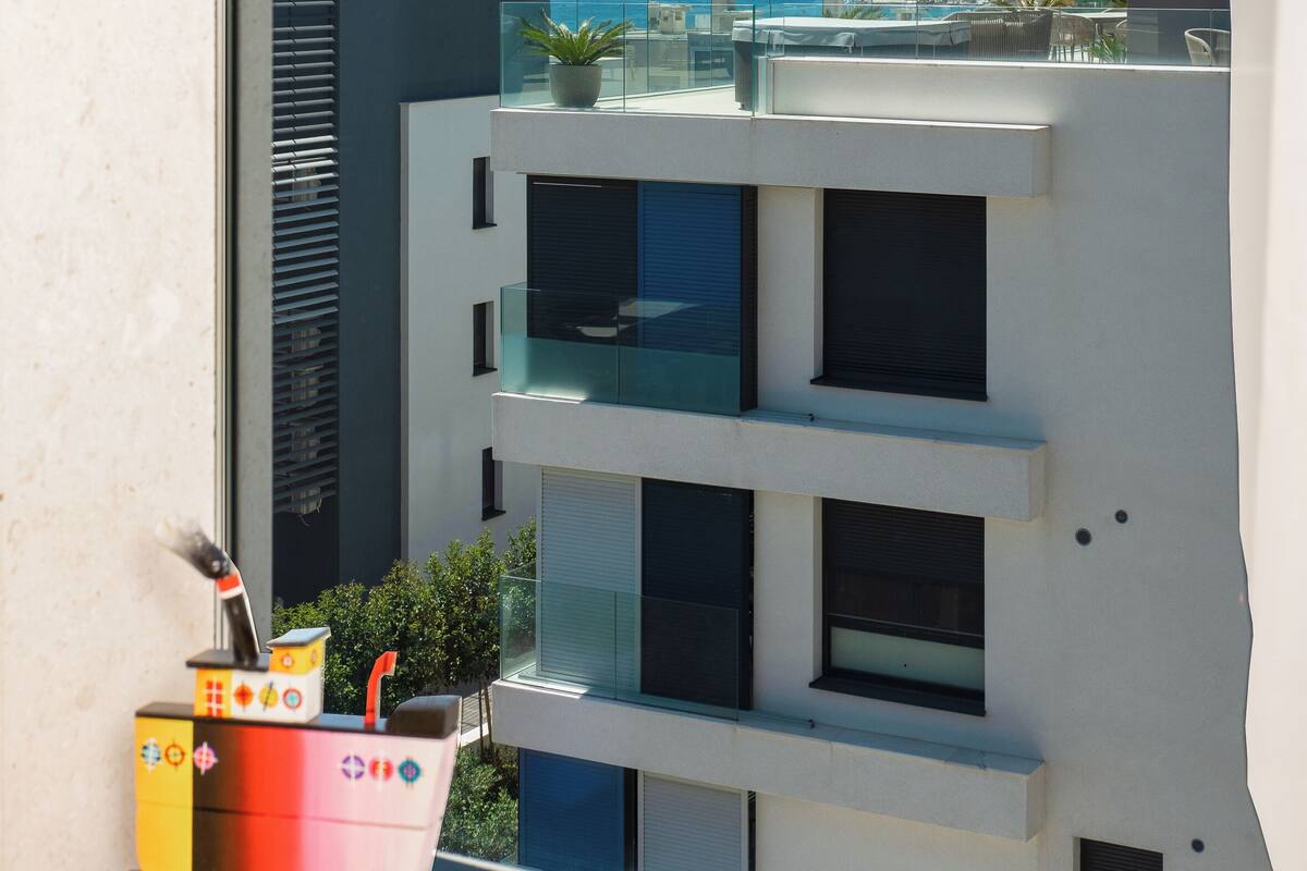 A modern building with a balcony overlooking a clear blue sky and a distant view of the sea.