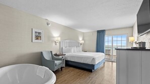 A hotel room with a bed, a chair, a bathtub, and a view of the sea through a large window. - The Baywatch Resort (Traverse City)