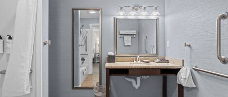 A modern bathroom with a sink, mirror, and handrails.