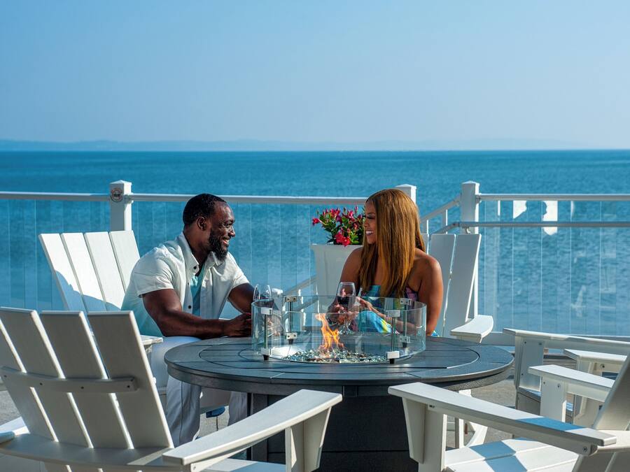 A couple dining at a table with a glass enclosure, overlooking a body of water.