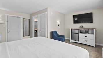Une chambre d’hôtel dotée d’un grand lit, d’un téléviseur fixé au mur, d’un minibar et d’un coin salon avec un fauteuil.