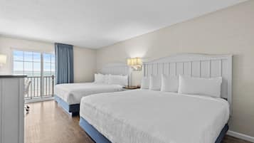 A hotel room with two beds, a balcony with a view, and a desk with a lamp.