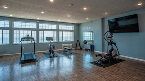 A spacious gym with multiple exercise machines, large windows, and a flat-screen TV on the wall. - The Baywatch Resort (Traverse City)