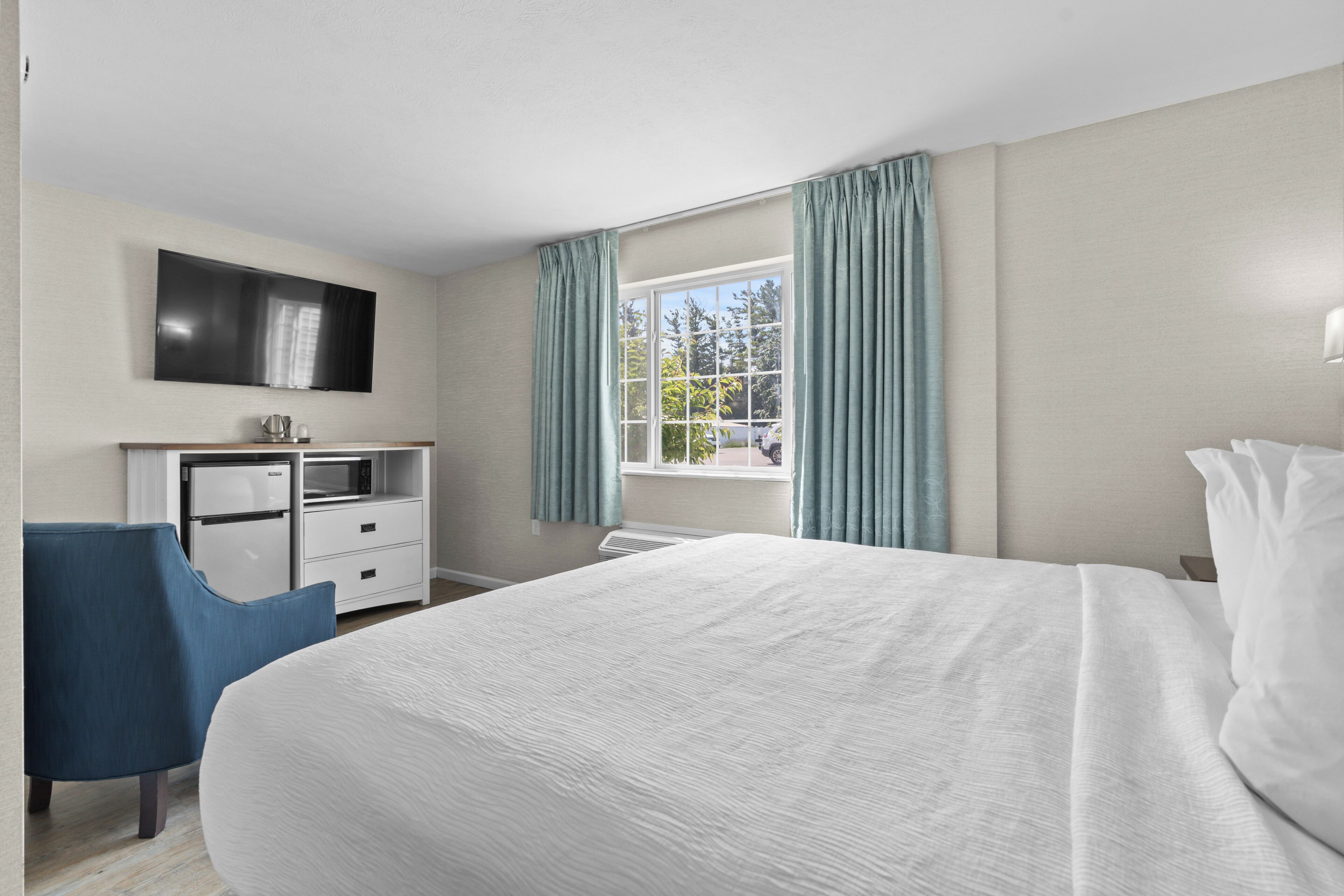 Une chambre d’hôtel avec un grand lit, un bureau doté d’un téléviseur à écran plat, une chaise et une fenêtre avec des rideaux.