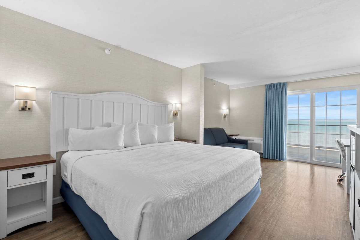 A hotel room with a large bed, a desk, a chair, and a view of the sea.