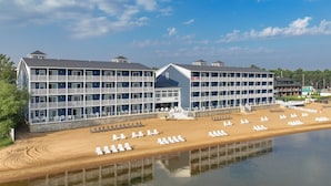 A large, multi-story hotel with a beachside location, featuring numerous balconies and a sandy beach with sun loungers. - The Baywatch Resort (Traverse City)