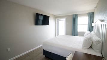A hotel room with a bed, a TV mounted on the wall, a window with curtains, and a wooden floor.
