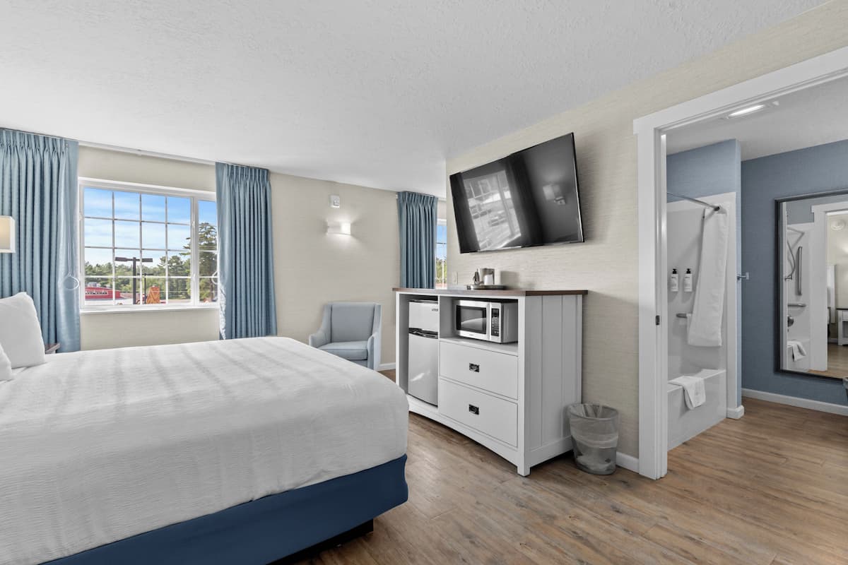 A modern hotel room with a large bed, a flat-screen TV mounted on the wall, a microwave, and a small trash bin.
