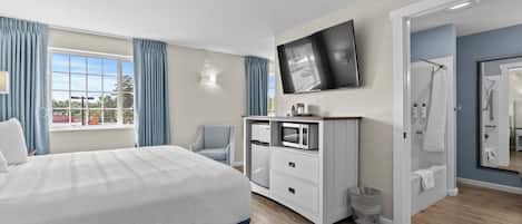 A modern hotel room with a large bed, a flat-screen TV mounted on the wall, a microwave, and a small trash bin.