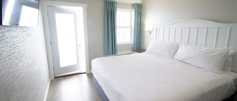 A hotel room with a large bed, a door leading to a balcony, and a window with curtains.