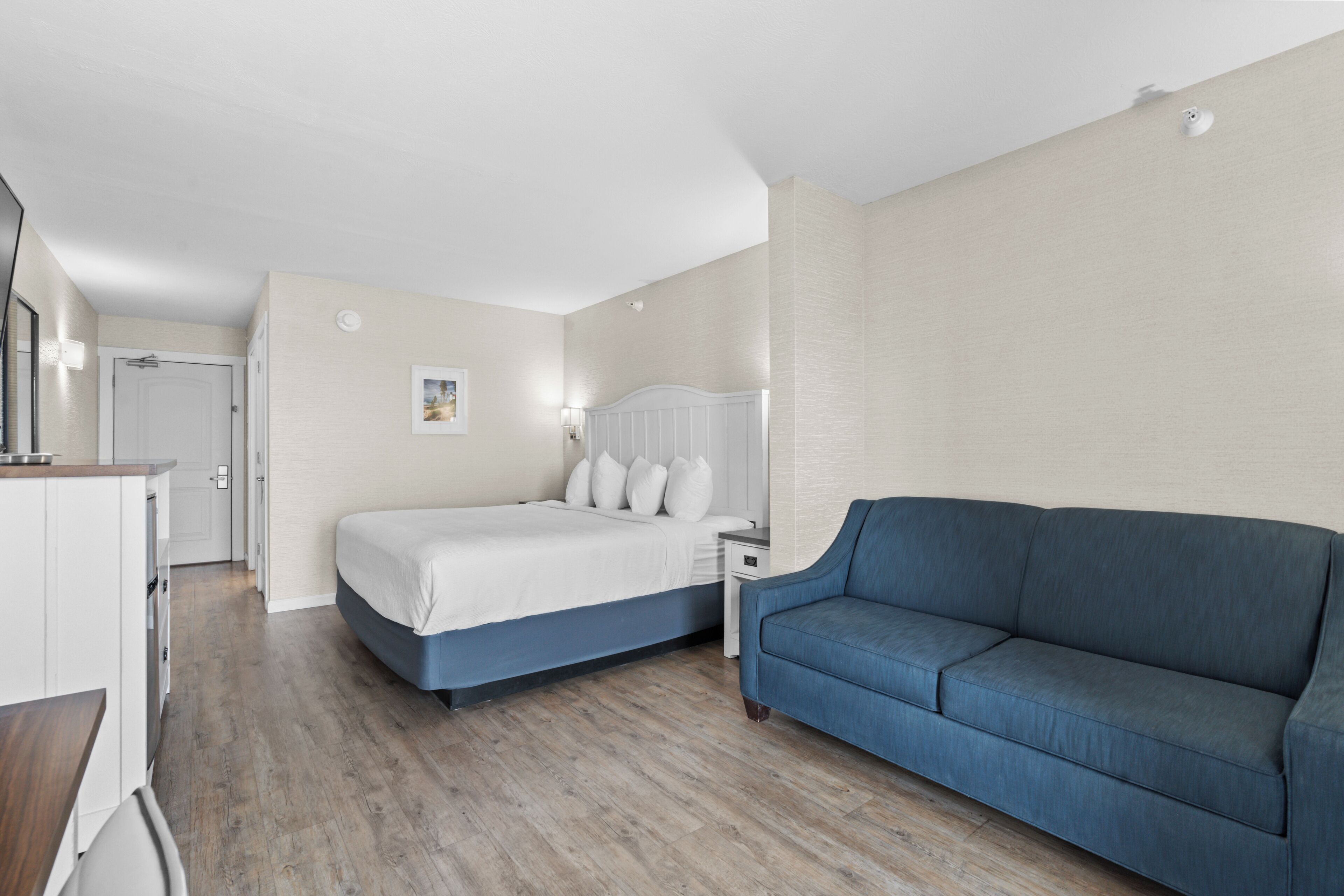 A bedroom with a bed, a blue sofa, a bedside table, and a nightstand.