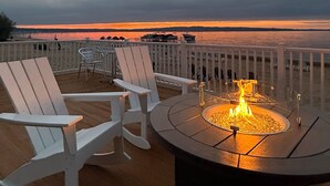 A deck with a fire pit and two chairs overlooking a sunset over water. - The Baywatch Resort (Traverse City)