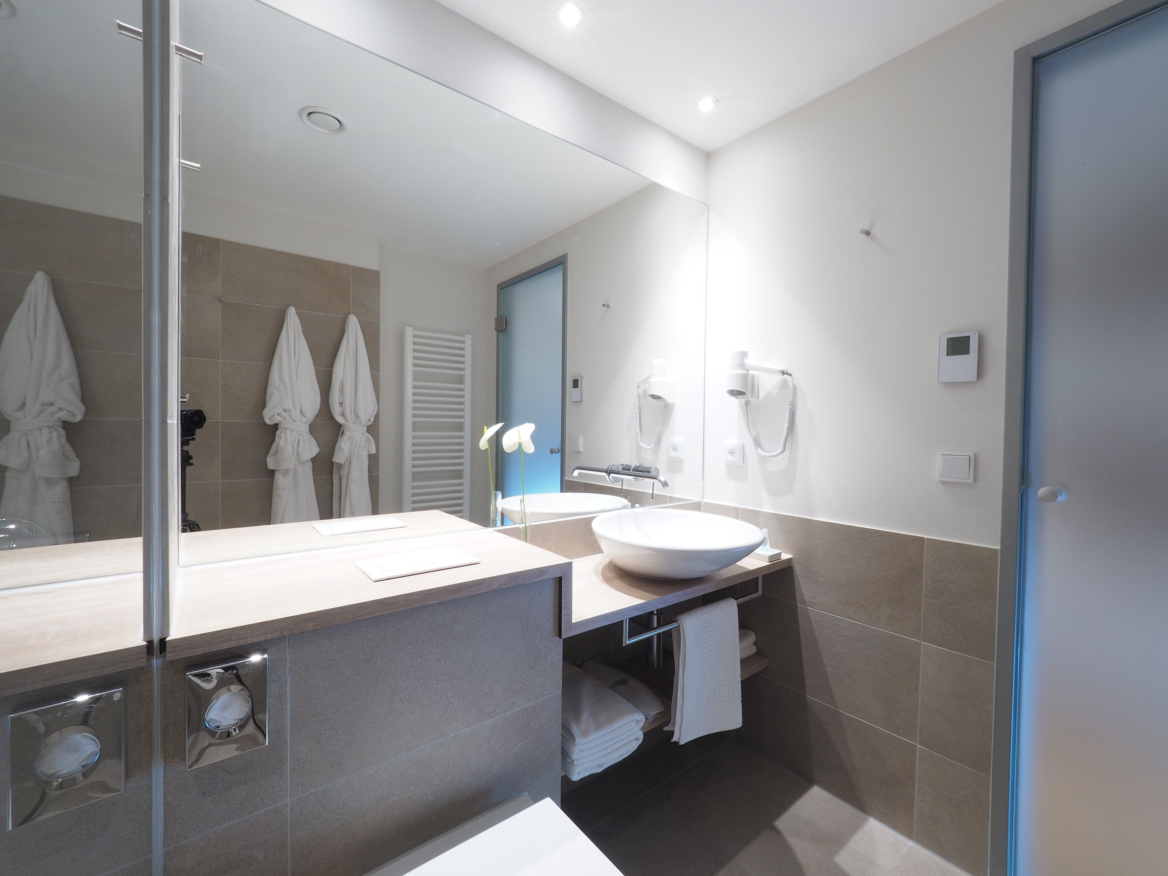 Een moderne badkamer met een grote spiegel, een witte wasbak en een handdoekhouder.