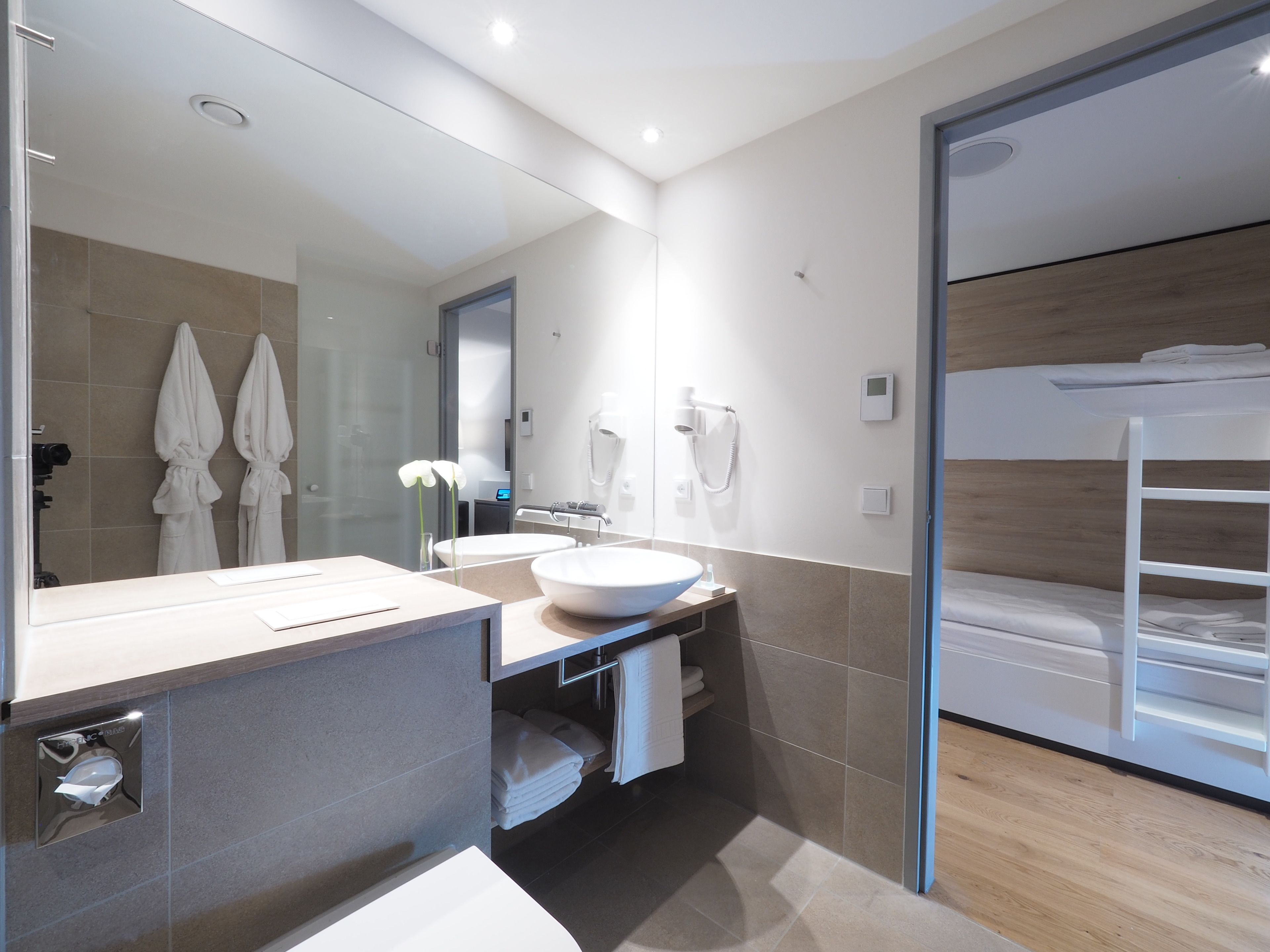 A modern bathroom with a large mirror, a sink, and a vanity. There are towels and a hairdryer on the wall.