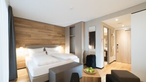 A modern hotel room with a large bed, bedside tables, a seating area, and a bathroom visible through an open door.