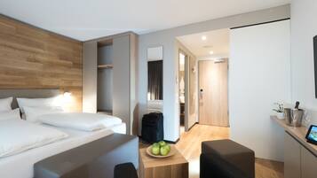 Ein modernes Hotelzimmer mit Bett, Schreibtisch, Äpfeln, Stuhl und Minibar.
