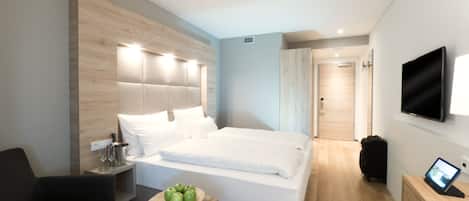 A modern hotel room with a large bed, bedside table, and a small round table with apples.